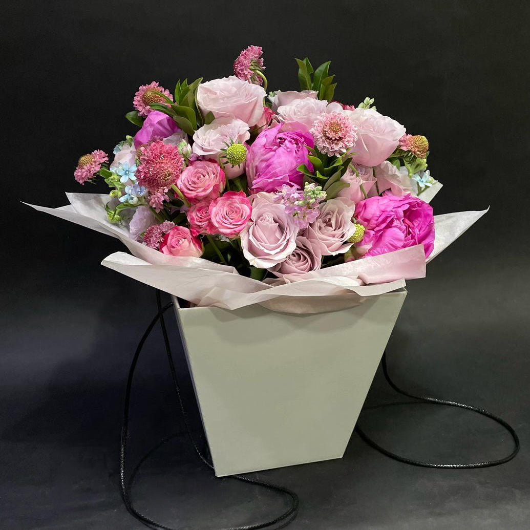 A chic Mother's Day bouquet featuring an assortment of pink roses and seasonal blooms in a stylish paper-wrapped pot.