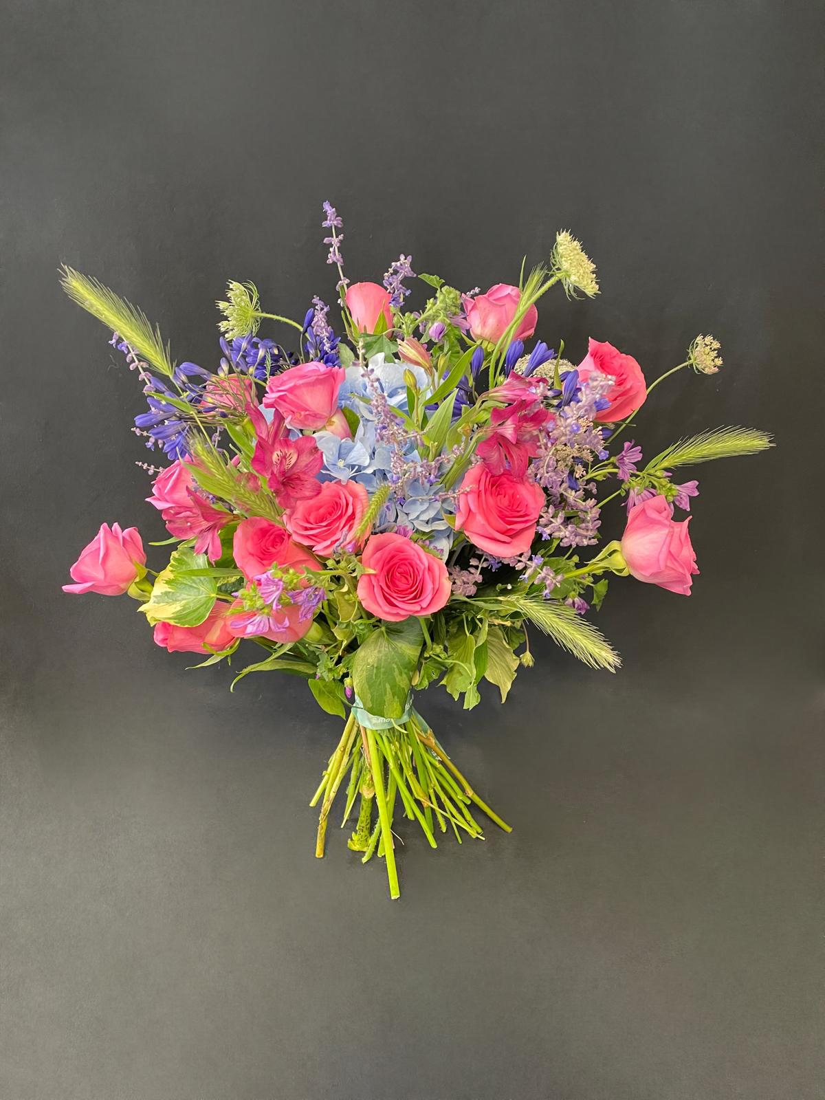 Hand-tied bouquet featuring vibrant pink roses, blue hydrangea, purple delphinium, lavender sprigs, and seasonal greenery — designed to uplift and brighten any recovery setting.