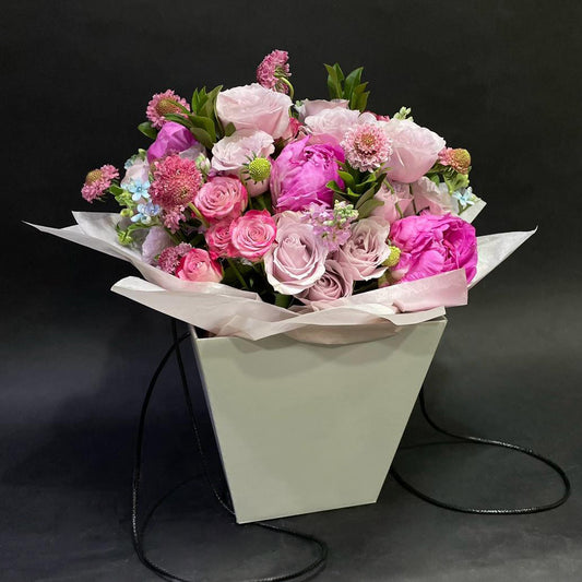 A chic Mother's Day bouquet featuring an assortment of pink roses and seasonal blooms in a stylish paper-wrapped pot.