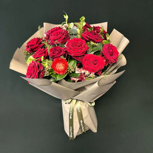 Luxurious bouquet of dark red roses tied with a branded ribbon, presented in a chic wrapping, perfect for Valentine's surprise.
